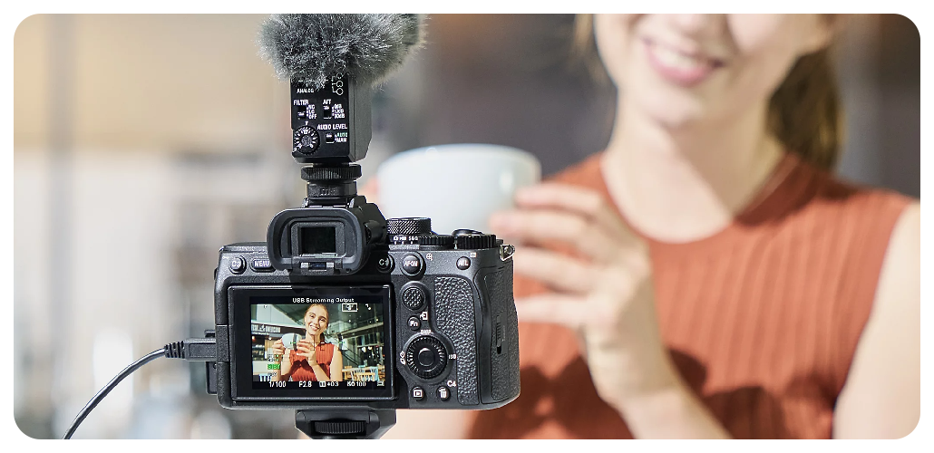 woman wearing muted oragne knitted vest holding coffee cup vlogging with Sony A7 IV camera